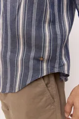Camisa de manga larga de lino con diseño a rayas en tonos celestes y blancos, cuello camisero clásico y cierre frontal de botones.