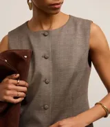 Chaleco regular color marrón claro con estampa de cuadros, confeccionado en punto roma, con cuello redondo, abotonado delantero con botones forrados y recorte en la bajo.