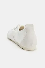 Zapatilla deportiva color blanco con detalles en gamuza y diseño de talonera elástica, cordones al tono y suela plana dentada.