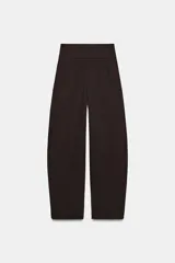 Pantalón negro de tiro alto, corte amplio estilo balloon o culotte, con pliegues marcados en el delantero y bolsillos laterales ocultos.