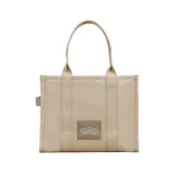 Bolso tote de gran tamaño Marc Jacobs, confeccionado en lona de algodón negra con el logo estampado en blanco en el frente. Cuenta con asas superiores reforzadas y una estructura amplia y resistente.