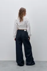 Jean wide leg negro de tiro alto, confeccionado en denim rígido, con diseño de cinco bolsillos, presillas para cinto, cierre frontal con botón y ruedo desflecado.