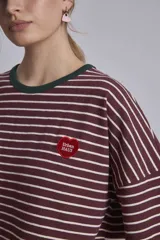 Remera oversize a rayas horizontales en tonos bordó y blanco, con cuello redondo verde oscuro y un pequeño parche bordado en forma de corazón en el pecho.