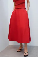 Falda midi de tiro alto y corte en A, color rojo, con bolsillos laterales ocultos y cierre lateral con cremallera.