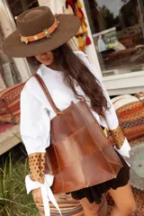 Bolso tote de cuero natural, confeccionado mediante la unión de piezas con costuras visibles y terminaciones artesanales. Cuenta con doble asa de hombro.