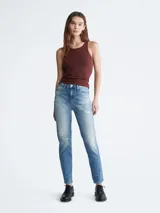 Jean de mezclilla azul claro con efecto lavado y zonas desgastadas/rotas en ambas piernas. Presenta un corte mom de talle alto, estilo clásico de cinco bolsillos y cierre de botón y cremallera.