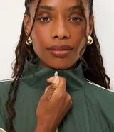 Campera rompeviento de diseño tricolor con bloques de color en verde, beige y blanco. Presenta cuello alto, cierre frontal con cremallera, mangas raglán y puños ajustados. El ruedo incluye un cordón regulable para un ajuste personalizado.