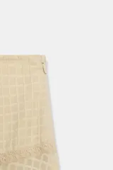 Falda larga de tiro medio en color beige, con tejido de textura cuadriculada. Presenta un diseño acampanado con detalle de costura horizontal y bajo acabado en volante. Cierre lateral con cremallera oculta.