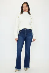 Pantalón de jean azul oscuro de corte flare con tiro alto. Presenta detalles de botones dorados en los laterales de la cintura y ruedo deshilachado.