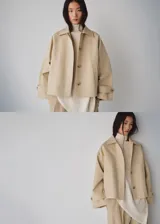 Chaqueta corta de algodón color beige, de corte holgado, con cuello clásico, cierre frontal de botones y bolsillos ribeteados. Cuenta con mangas largas amplias con puños ajustables mediante tiras y botones.