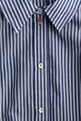 Vestido midi camisero con estampado de rayas verticales en tonos azul y blanco, cuello camisero, botonadura frontal y mangas cortas. Incluye un cinturón para anudar en la cintura y falda de corte acampanado.