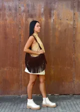 Cartera de hombro tipo hobo confeccionada en cuero gamuzado color chocolate, con detalle de flecos largos en la parte inferior y correa ajustable con hebilla metálica.