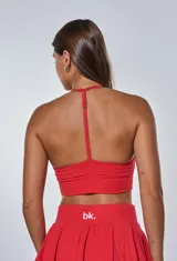 Conjunto deportivo compuesto por un top con escote en V y espalda deportiva, y una pollera short con diseño plisado. El top presenta el logo de la marca estampado en el frente.