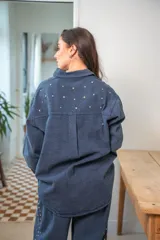 Camisa de denim negra con botones metálicos dorados y bolsillos con tachas doradas. De corte amplio.