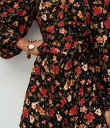 Enterito corto de viscosa con estampado floral sobre fondo negro, escote en V, mangas largas con volumen y puños ajustados.