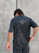Remera gris con efecto lavado, corte oversize y estampa en la espalda con texto y logo.