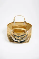 Bolso tipo tote de Bimba y Lola, color dorado con acabado metalizado y efecto arrugado. Presenta un diseño cuadrado con estampado central de la marca en un recuadro oscuro y doble asa de mano en color crema.
