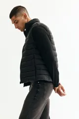 Chaleco acolchado de nylon rompevientos, color negro, con diseño guateado, cuello elevado y cierre frontal. Cuenta con bolsillos laterales con cierre y forro interior.
