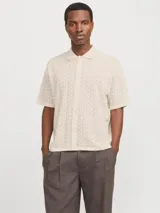Polo loose de tejido estructurado color beige, con cuello tipo polo, mangas cortas, hombros caídos y cierre frontal con botones.