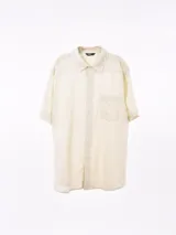 Camisa de manga corta color negro, con cuello camisero y un bolsillo de parche en el pecho izquierdo. Presenta un corte holgado (oversize).