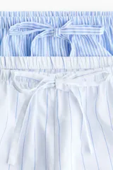 Pack de dos shorts de pijama con cintura elástica, cordón ajustable y aberturas laterales en el dobladillo. Uno presenta diseño a rayas celestes y blancas, y el otro diseño a rayas blancas y celestes.