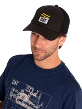 Gorro tipo trucker de color negro con malla en la parte posterior. Presenta un parche frontal con el logo de Caterpillar y diseño de placa de diamante. Cuenta con visera curva y cierre ajustable con broche.