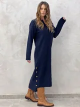 Vestido midi de punto color azul marino, con cuello en V, mangas largas y diseño holgado. Presenta un patrón de rombos en relieve y aberturas laterales con botones decorativos en el ruedo.