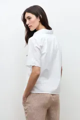 Camisa blanca de manga corta con sutiles detalles bordados tonales, cierre frontal de botones y cuello camisero.