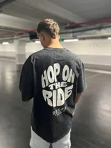 Remera negra con efecto lavado, de corte relajado y caída amplia. Presenta una estampa tipográfica "Hop On The Ride" en blanco y de gran tamaño en la espalda, y un mini logo "Dropz" en el pecho.