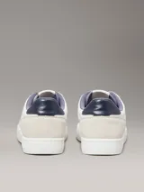 Zapatillas de corte bajo Calvin Klein, con diseño minimalista en color blanco y beige. Presentan una combinación de materiales en la capellada, incluyendo piel y ante, con detalles en contraste en el talón y logo de la marca en el lateral y la mediasuela.