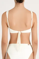 Top de bikini bandeau color crema, con fruncidos en las copas y un aro metálico central decorado con abalorios dorados. Cuenta con tirantes anchos.