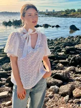 Blusa blanca de algodón bordado con cuello con volados y lazo.