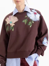 Buzo de corte oversize color marrón chocolate, con cuello redondo y diseño estampado de flores en la parte frontal. Presenta mangas largas con puños ajustados.
