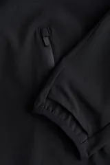 Campera deportiva de running color negro, confeccionada en tejido funcional DryMove. Presenta un diseño de corte holgado con medio cierre frontal, capucha de doble capa, mangas raglán con abertura para el pulgar y bolsillos laterales con cierre. Incluye cordón elástico ajustable en el bajo y detalles reflectantes.