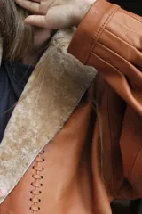 Campera oversize de cuero tostado con solapas y forro interno de corderito sintético azul marino, mangas anchas y detalles de costuras trenzadas.