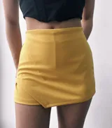 Short pollera color mostaza, de tiro alto con corte asimétrico.