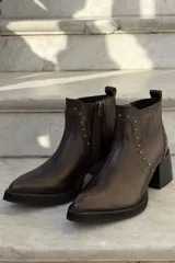 Bota corta de cuero color bordó, con taco cuadrado negro y suela de plataforma. Presenta detalles de tachas metálicas plateadas a lo largo de la costura frontal y lateral, con cierre interno.