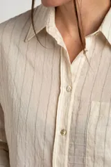 Camisa de manga larga con patrón de rayas sutiles, corte holgado, cuello camisero, cierre frontal con botones y un bolsillo aplicado en el pecho.