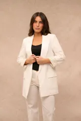 Blazer blanco de corte recto y largo medio, con solapas clásicas, bolsillos con solapa en el frente y mangas largas con vuelta estampada a rayas.