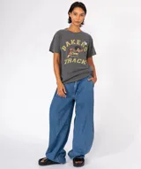 Remera de algodón color azul grisáceo con lavado especial, cuello redondo y manga corta. Estampado frontal con el texto "Bakers Track" y un personaje de pato de dibujos animados saltando un obstáculo.