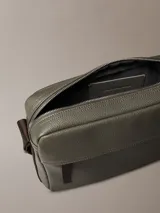 Bolso bandolera Calvin Klein de cuero sintético texturizado color verde oliva, con correa ajustable de tela marrón oscuro que lleva el logo de la marca repetido. Presenta un bolsillo frontal horizontal y el logo CK grabado en la parte inferior derecha.