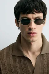 Polo de punto color marrón oscuro, de calce regular, con cuello solapa y abertura frontal en V. Presenta tejido con trencitas verticales.