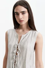 Blusa sin mangas color gris claro con textura rayada vertical y lazo ajustable en el escote.
