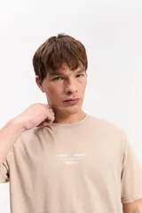 Remera de algodón color marrón con efecto gastado, de manga corta, cuello redondo y estampa tipográfica sutil al frente.