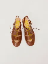 Sandalias planas tipo slingback de cuero marrón, con diseño delantero calado, cierre de cordones y tira trasera ajustable con hebilla.
