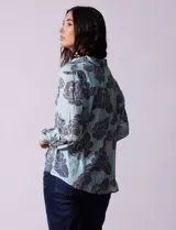 Blusa celeste con estampado de flores grises, de gasa, con cuello con solapa y escote en V, abertura central con botones, bolsillo aplicado y terminación anudada.