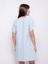 Vestido corto de corte holgado, color celeste, con cuello redondo fruncido y mangas cortas. Está confeccionado en una tela con textura diferenciada que le aporta relieve.