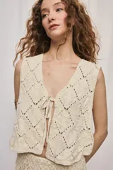 Chaleco corto de algodón color beige, confeccionado con un diseño calado en rombos, escote en V y cierre frontal con lazo para anudar.