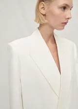 Blazer de corte recto y estilo sastre, color blanco, con cuello de solapa, cierre frontal de botón oculto y bolsillos laterales de ribete.