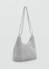 Bolso de mano tipo baguette con diseño estructurado, recubierto completamente por cristales facetados sobre una base de aluminio. Cuenta con doble asa de cadena metálica, cierre superior de cremallera y forro interior de poliéster.